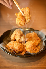 Warm tone with hot fried chicken and chopsticks in black dish on the wooden table.