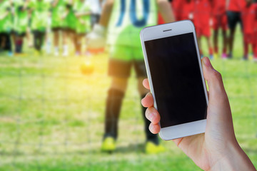 hand holding smartphone with young boy as a soccer goalkeeper during football match ready to save.