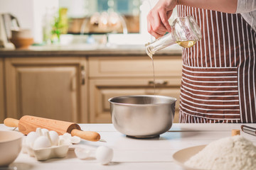 Young woman pouring oil into a bowl with dough, close-up