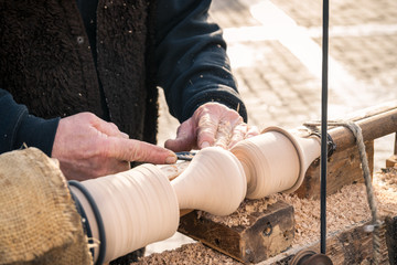 An artisan carves a piece of wood using a manual lathe.