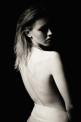 Dramatic portrait of sad young woman among the dark. Rear view, black and white