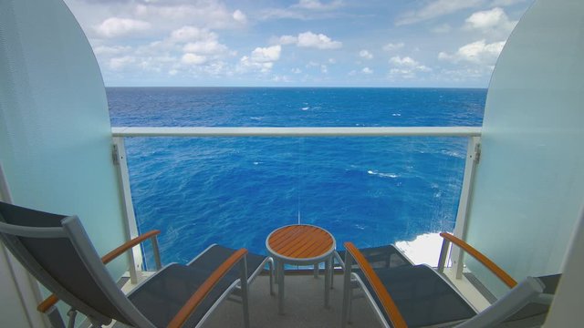 Cruise Ship Balcony with Furniture View Sailing on Tropical Water with Passing Waves during an Idyllic Day with White Clouds in a Blue Sky