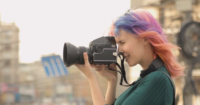 Pretty girl doing photos on old camera and smiling in the city