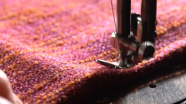 An elderly woman seamstress sews a cloth on an old sewing machine. Close-up. Slow motion