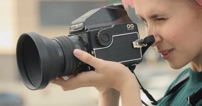 Pretty girl doing photos on old camera and smiling in the city