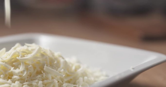 Slide shot of grated pizza mozzarella cheese falls in plate, 4k 60fps prores footage