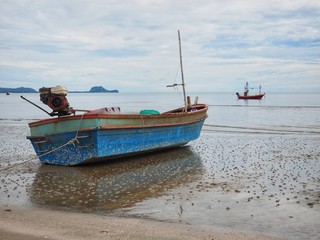 Obraz premium Fishing boat parking on sand beach with beautiful clam sea background on cloudy day, dolphin bay, prachuap khiri khan, Thailand