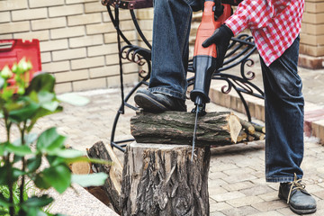man in plaid shirt sawing piece of wood on stump