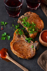 Juicy grilled pork steak with pesto sauce and tomato sauce on a black background