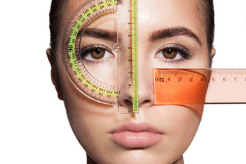 The woman's face is measured with colored rulers before the plastic surgery to change the...