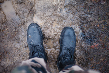 Army boots on dirty and damp earth at sunset