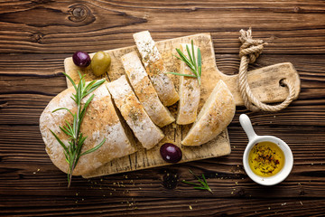 Delicious homemade italian ciabatta bread with olive oil and olives on wooden rustic background, above view - obrazy, fototapety, plakaty