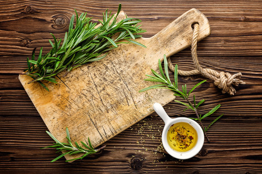 Culinary background with wooden board and cooking ingredients, olive oil and rosemary, above view, space for a text