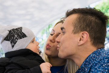 A happy married couple is sitting in a cafe and enjoying this time. They play with their child, he smiles.