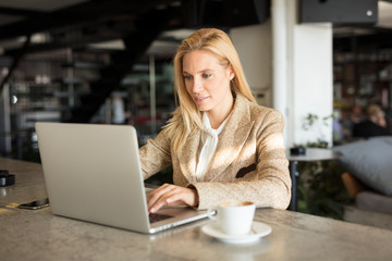 Modern business woman in city cafe. Drinking coffee and surfing the web.