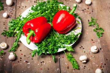 Two red bell peppers with fresh herbs and spices on wooden background. Rustic take..