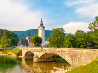 Church of St John the Baptist and old stone bridge at Lake Bohinj in alpine village Ribicev Laz,...