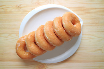 Top view of lined up sugar-glazed doughnuts served on white plate and on the wooden table 