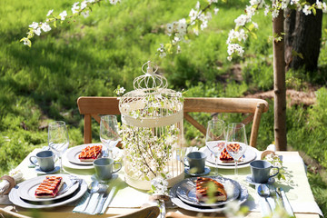 Beautiful table setting and cage with flowers in garden