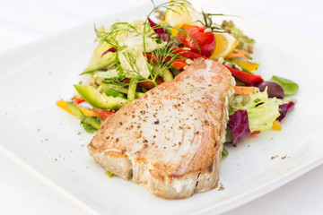 Tuna steak with colorful vegetables served in a restaurant, white background.