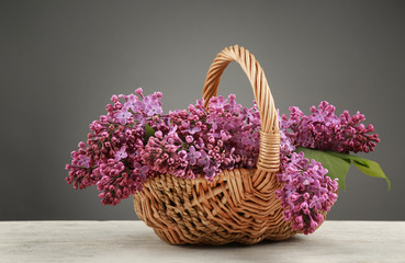 Fototapeta premium Wicker basket with beautiful bouquet of lilac flowers on light table