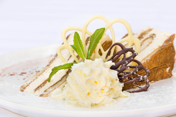 Slice of classic tiramisu cake in modern serving in a restaurant. White and dark chocolate decoration on the plate.