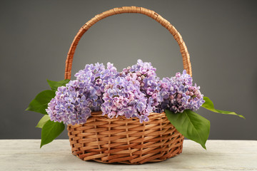 Wicker basket with beautiful bouquet of lilac flowers on light table