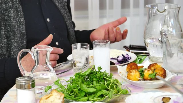 Friends drinking raki at counter in home, chatting with spouse. Close up. Raki, mastika and ouzo are aniseed flavored drinks, related to arak, most popular in Turkey