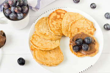 Top view of pancakes placed round on white table with blueberries .