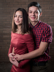 Happy young couple in love stand and smile in a red brick studio