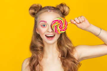 Happy young woman with big colorful lollipop over yellow background. Young and funny teenager girl.