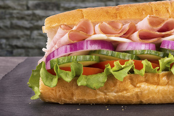 Close up on submarine ham sandwich, brick wall in background.