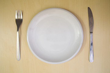 Empty plate, fork and knife on a wooden background. Top view
