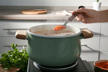 Female hand holding spoon with lentil above pan in kitchen