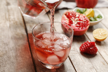 Pouring cold fruit cocktail into glass on wooden table, closeup