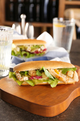 Wooden board with chicken salad in hot dog bun on table