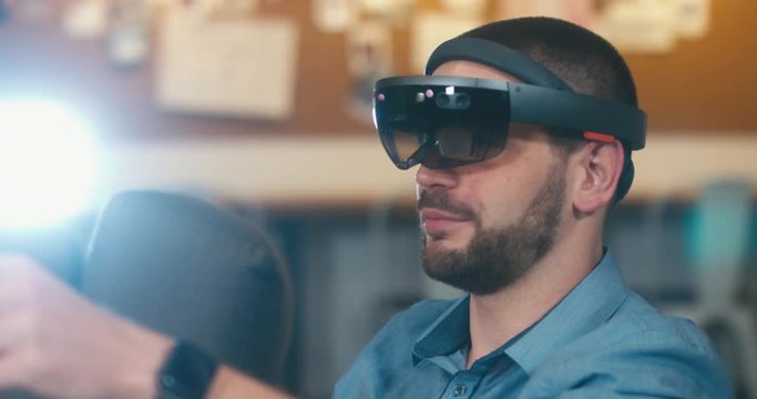 CU young adult Caucasian male using holographic augmented reality glasses in trendy office. Future concept. 4K UHD RAW edited footage