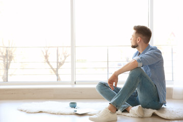Happy young man sitting on floor near window