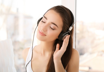 Beautiful young woman with headphones near window