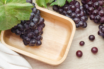 Fresh grapes with leaves in wooden bowl on table background.