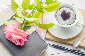 Notebooks, pen and chocolate cake in a cup with rose flower on white wooden background. flower on white wooden background.