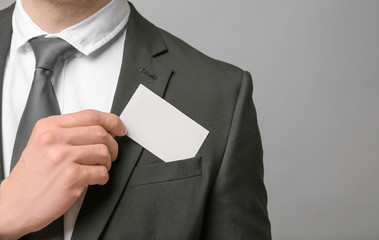 Handsome young man with business card on grey background, closeup