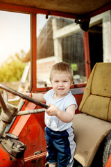 Baby boy holding a steering wheel of tractor. Childhood moments on the countryside.