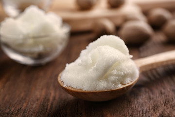 Shea butter in spoon on wooden background, close up
