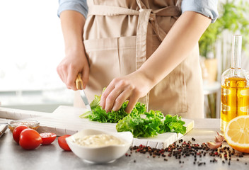 Obraz na płótnie Canvas Woman cutting lettuce on kitchen table