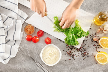 Woman cutting lettuce on kitchen table, top view