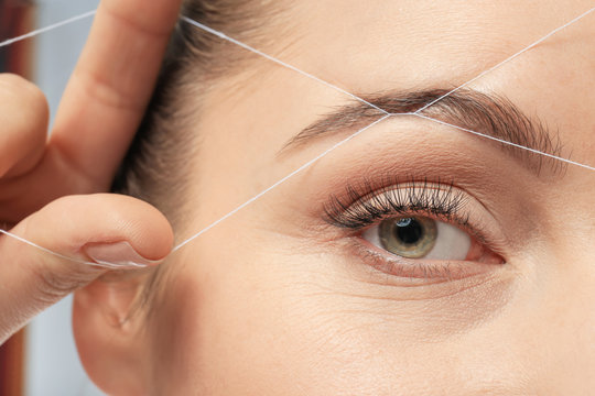 Young woman correcting shape of eyebrow with thread, closeup