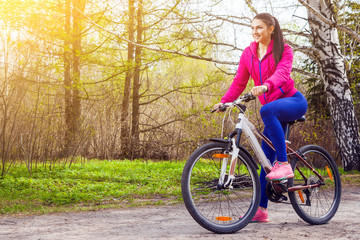 Naklejka premium Young woman rides a bike along a path in the forest at sunset of a summer day