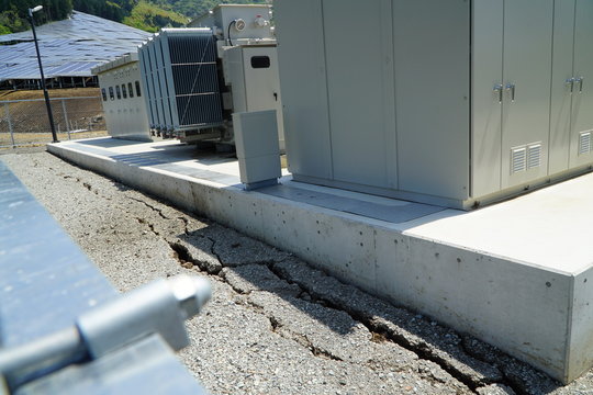 熊本地震で陥没した太陽光発電所の変電設備と
 奥に見える散乱した発電パネル