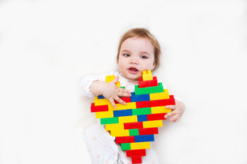 baby cute girl holds heart with lots of colorful plastic blocks constructor. Love heart for valentine background. .